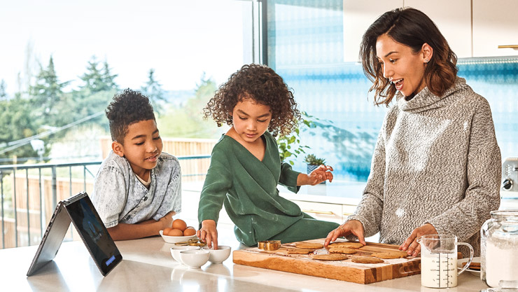 Mutter und ihre Kinder backen Kekse, während sie mit ihrem Windows 10-Computer interagieren