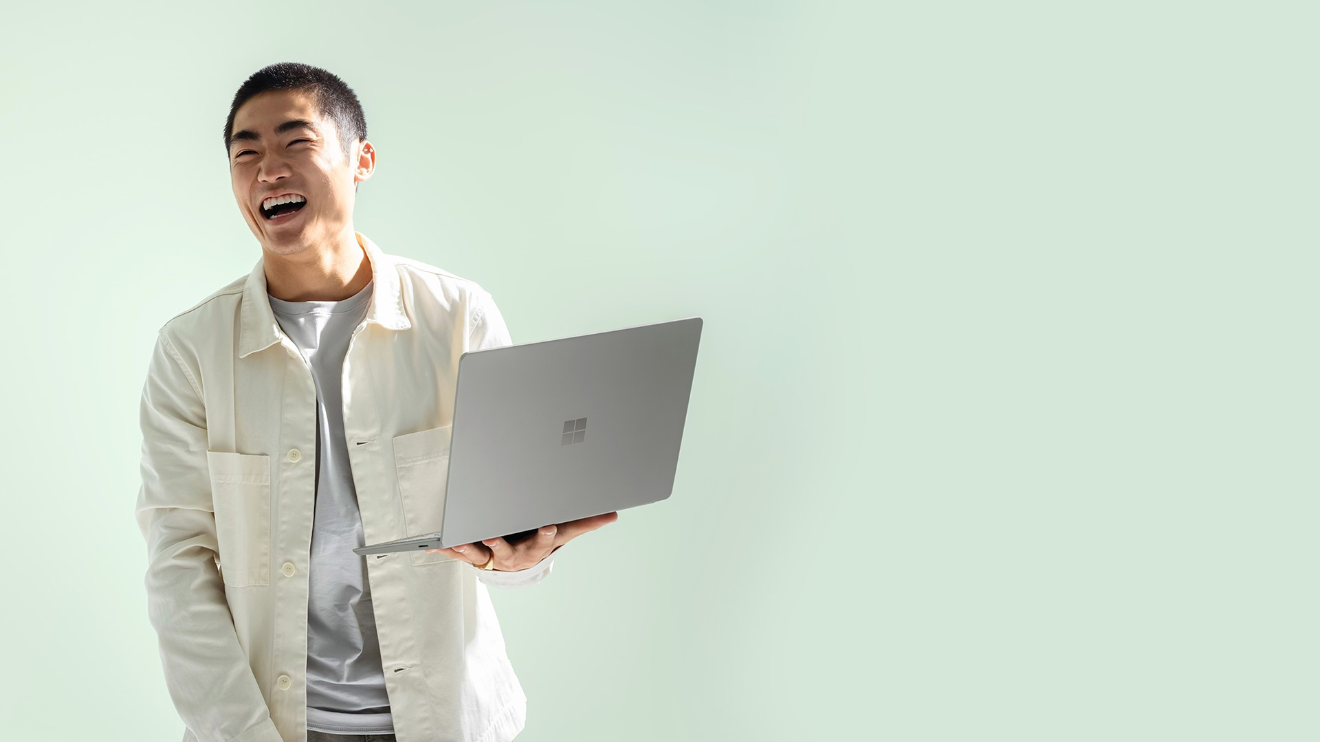 A man laughs holding his Surface Laptop Go 2 in sage.