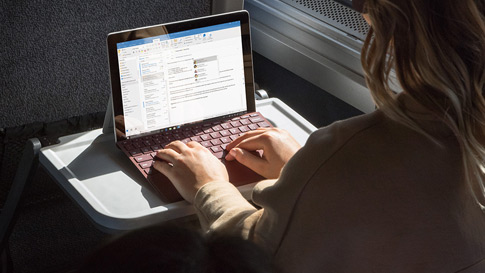A woman works on Surface Go with Surface Go Signature Type Cover on a train