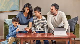 Man, woman, and 2 boys using two Microsoft Surface computers while sitting on a couch at home