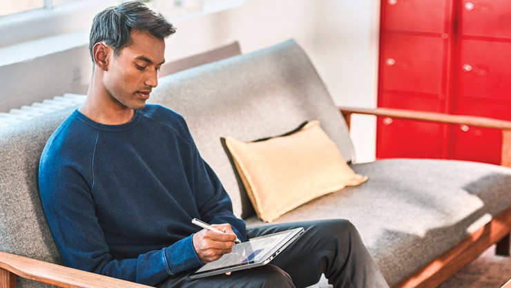 Man sitting on a sofa using a digital pen to interact with his Windows 10 computer
