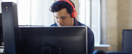 A man wearing headphones working at a desktop PC. Office 365 simplifies IT.