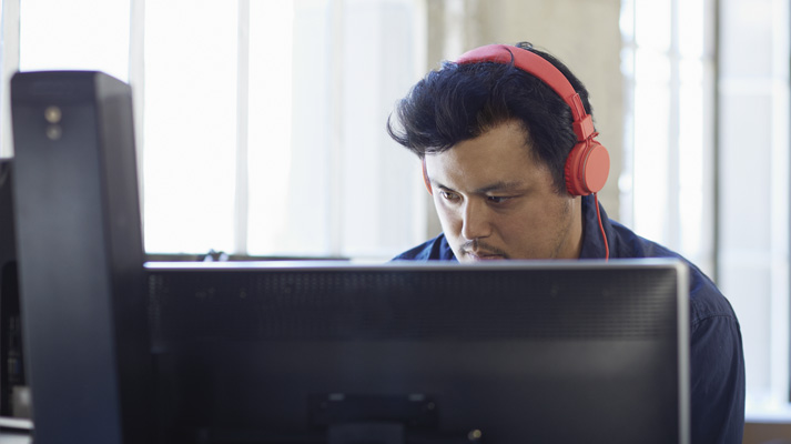 A man wearing headphones working at a desktop PC. Office 365 simplifies IT.
