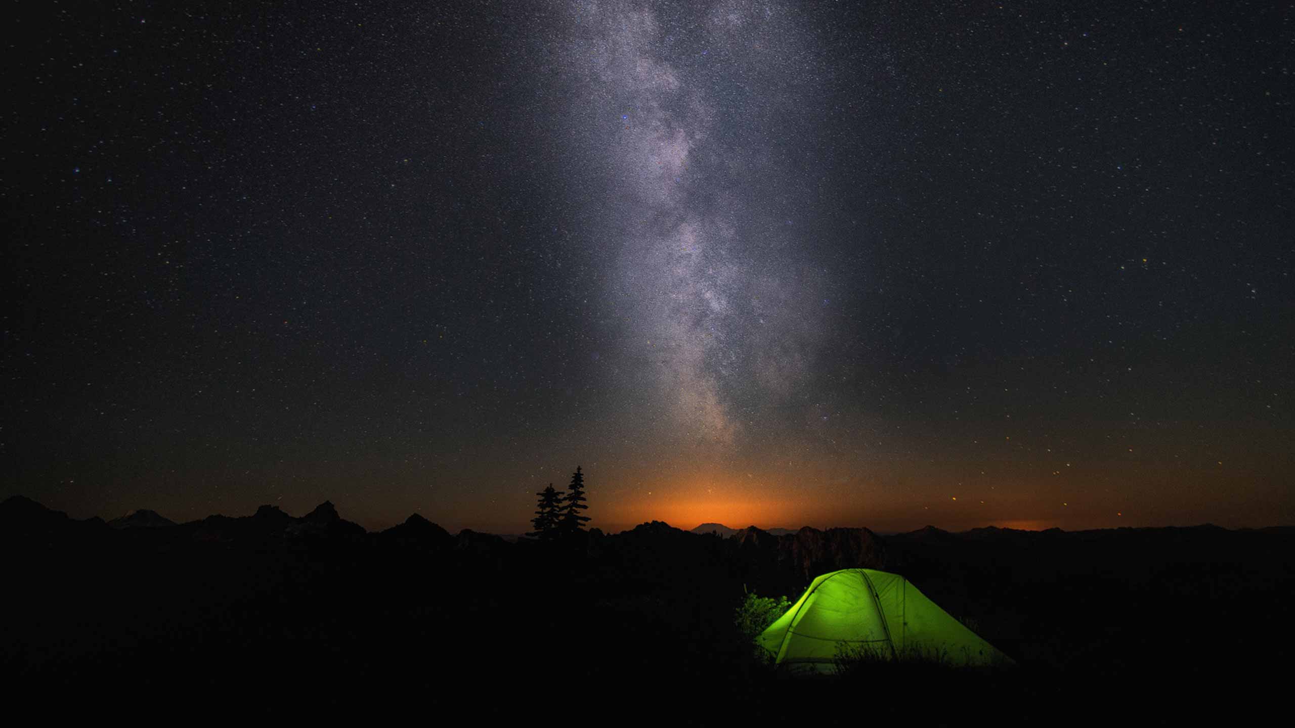 A green tent below the Milky Way in a dark night sky