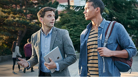 Two men walking and talking with one clutching a back pack and the other holding a Surface Pro 4