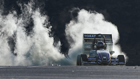 Image of Formula type racecar spinning its wheels and smoke rising behind it 