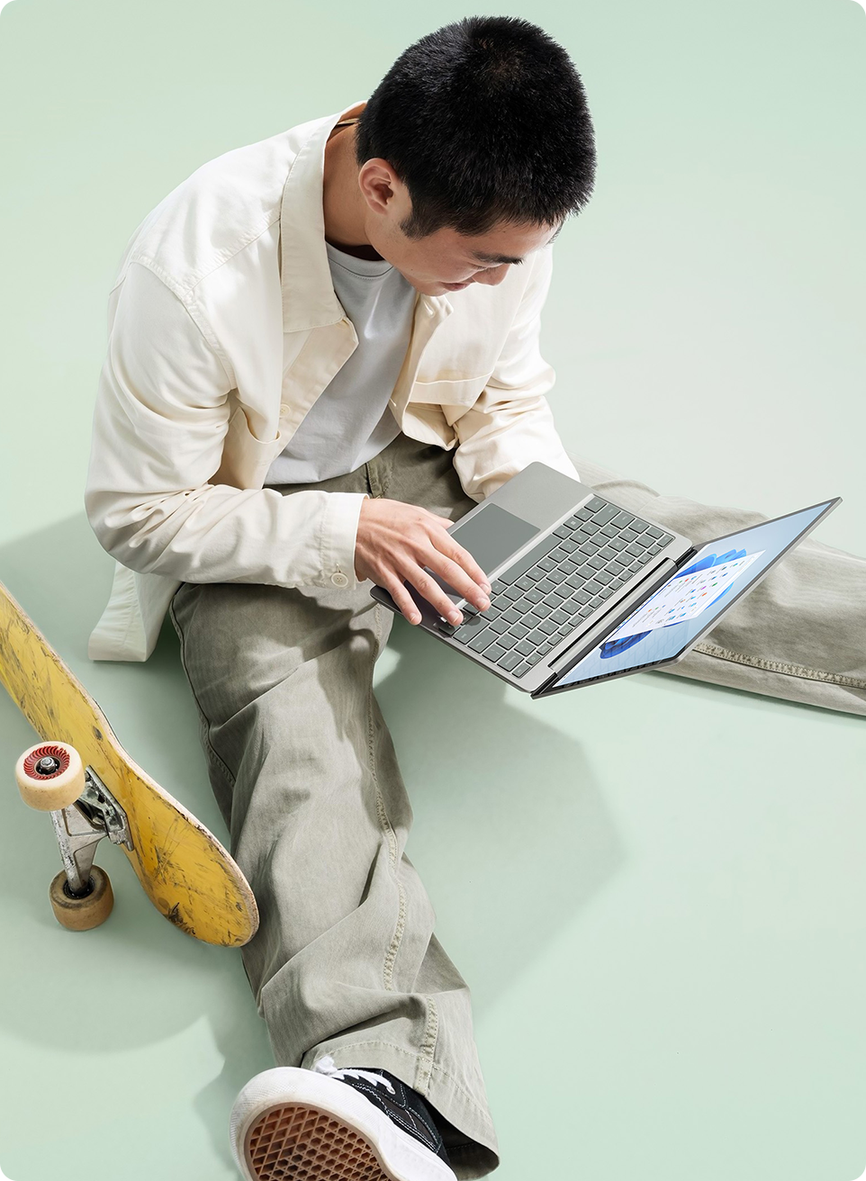 A young man takes a break from skateboarding to type a quick message on Surface Laptop Go 2.