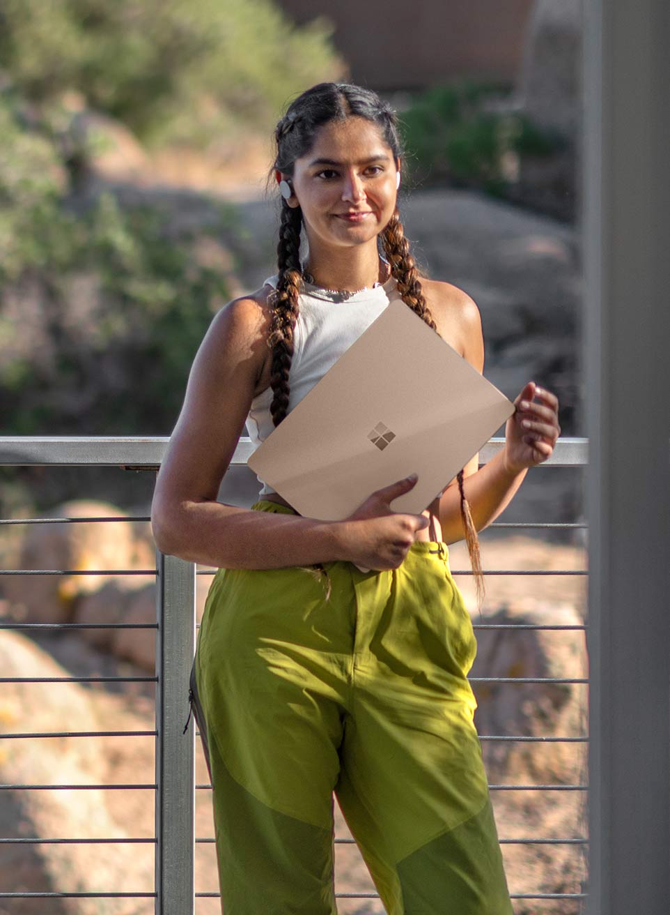 A woman with long braids holds her Surface Laptop 5 in Sandstone standing in front of a desert background.