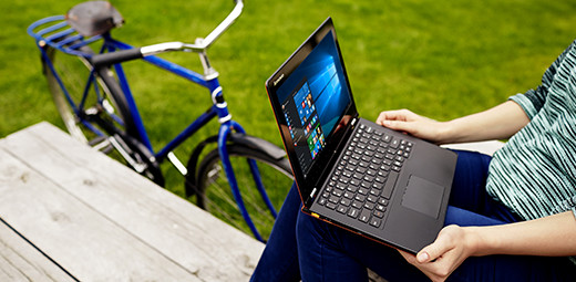 A person on a picnic table holding a Windows 10 laptop on their lap