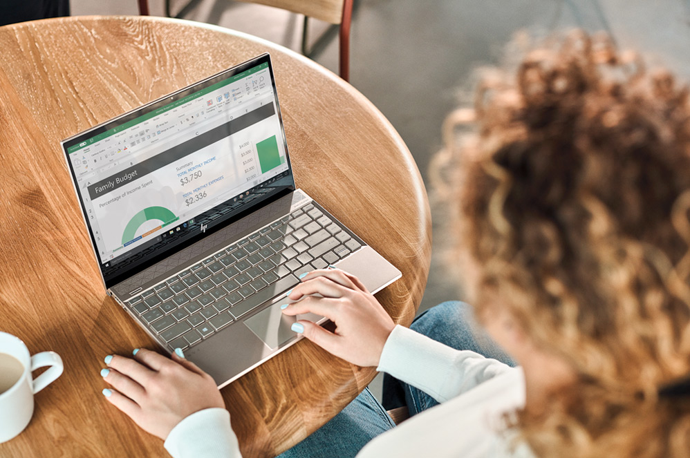 Mujer sentada en una mesa con una pantalla de Excel en su portátil