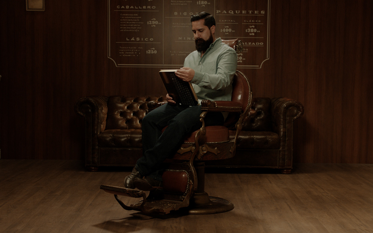 Marco sentado en una silla de barbería usando la HP Pavilion x360 como tableta.