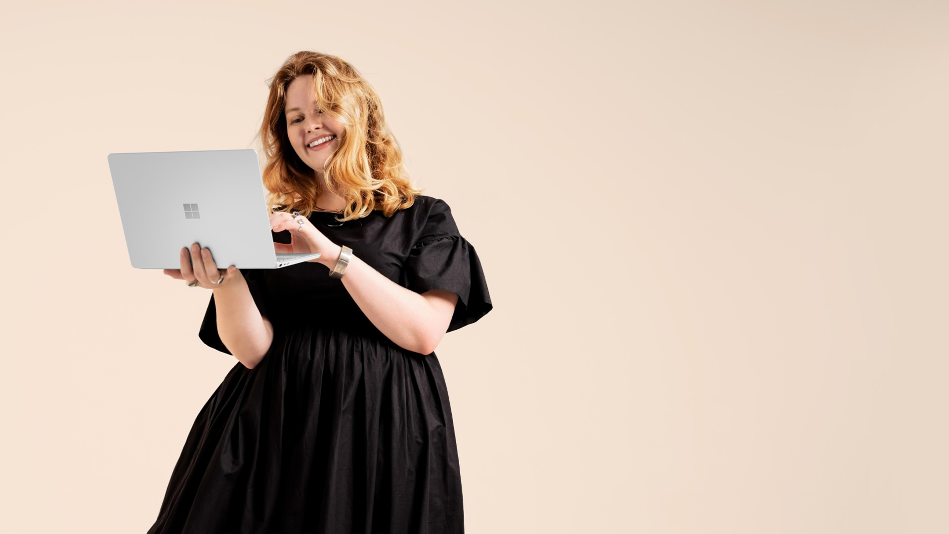 Egy nevető nő platina színű Surface Laptop Go 2 készüléket tart a kezében kinyitva, írásra készen.