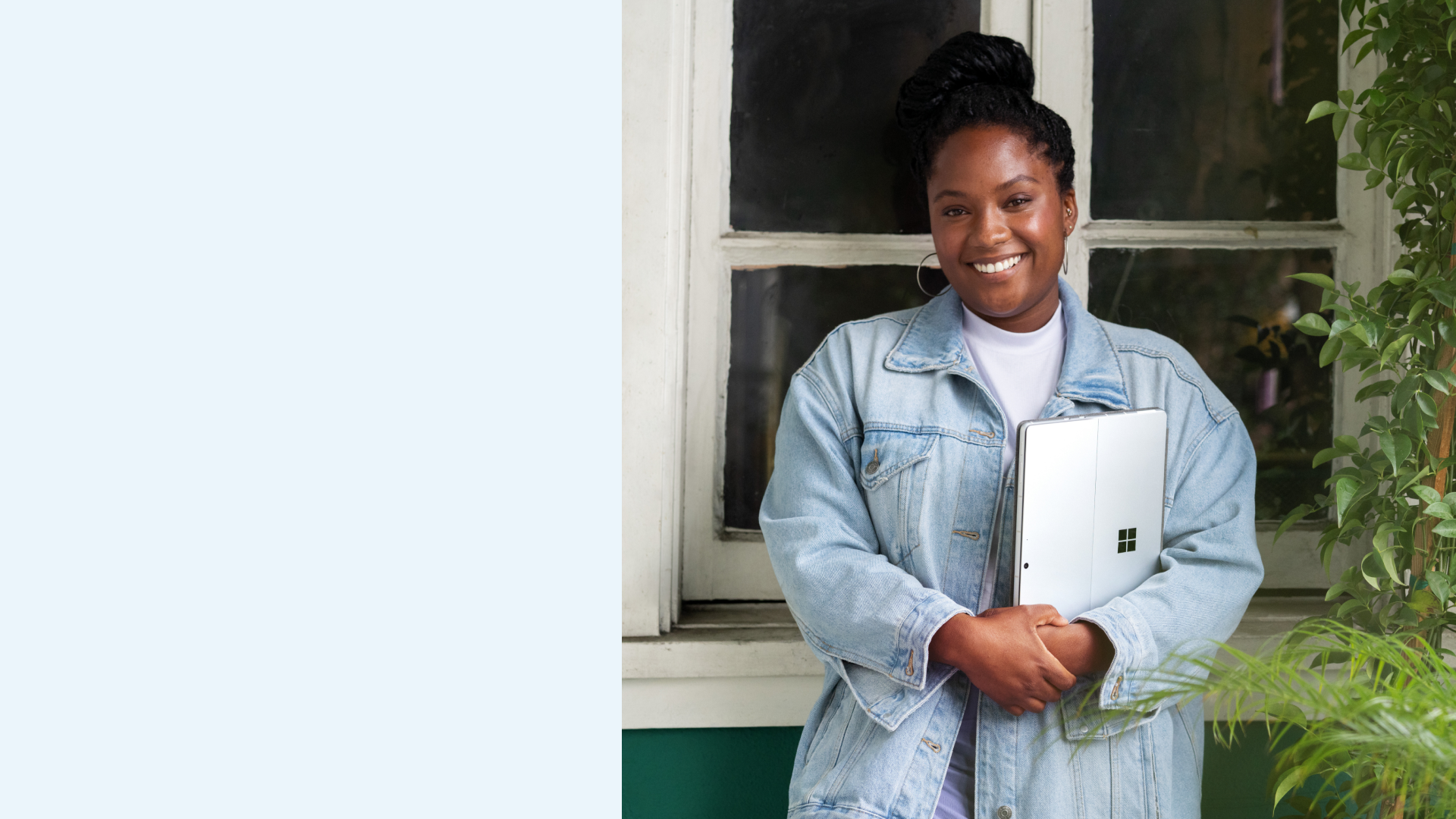 Uśmiechnięta kobieta pozująca do zdjęcia na tle okna i trzymająca platynowy komputer Surface Pro 9.