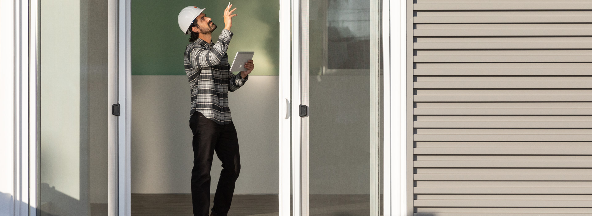 Un lucrător purtând o cască de protecție într-un cadru rezidențial și ținând un dispozitiv Surface Go 2 în modul tabletă