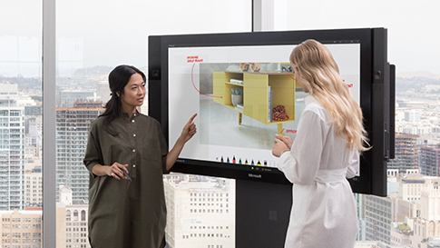 Två kvinnor som använder pekskärmen på en Surface Hub, och som använder Microsoft Whiteboard för att göra en designritning.